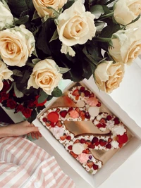 Elegant bouquet of pale yellow and deep red roses beside a beautifully decorated cake adorned with heart-shaped accents.