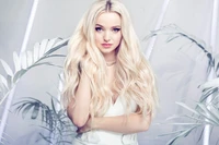 Dove Cameron dans une séance photo captivante, mettant en valeur ses longs cheveux blonds sur fond de design moderne et épuré, entouré de verdure luxuriante.