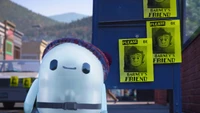 Un personnage animé fantaisiste portant un bonnet en tricot se tient à côté d'affiches cherchant de l'amitié pour Barney, dans une ville colorée.