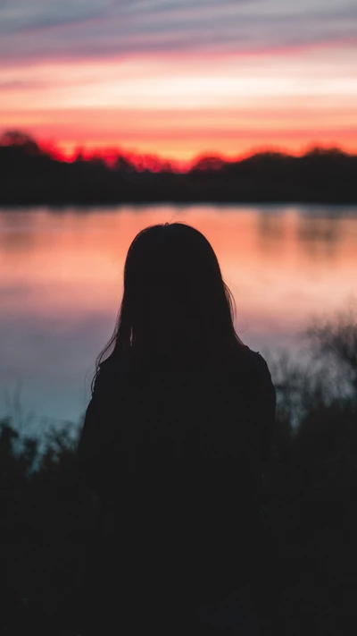 Solidão ao pôr do sol: Uma silhueta à beira do lago tranquilo