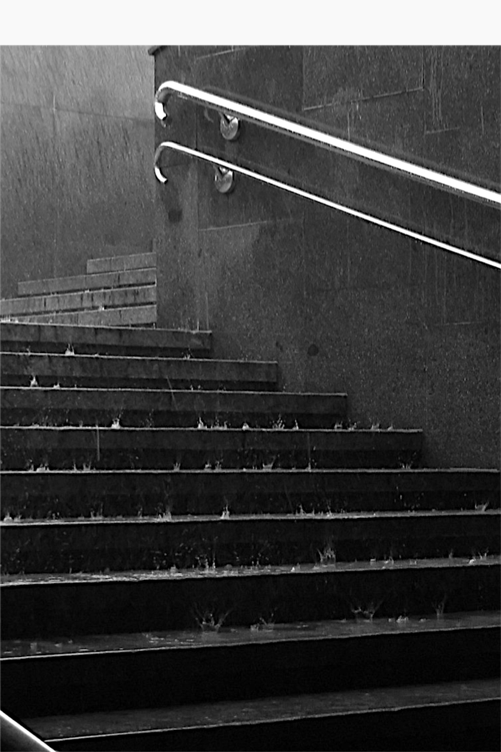 Hay un hombre montando un patineta por un conjunto de escaleras (blanco y negro, lluvia, escalera)