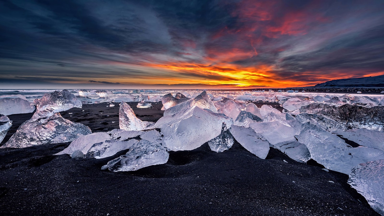 Um grupo de icebergs em cima de uma praia sob um céu nublado. (ilha, gelo, neve, inverno, por do sol)