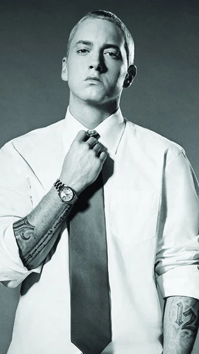 Eminem in einem Hemd und einer Krawatte, die seine Tattoos zeigt und eine selbstbewusste Pose einnimmt, verkörpert die Fusion von Hip-Hop und Gentleman-Stil.