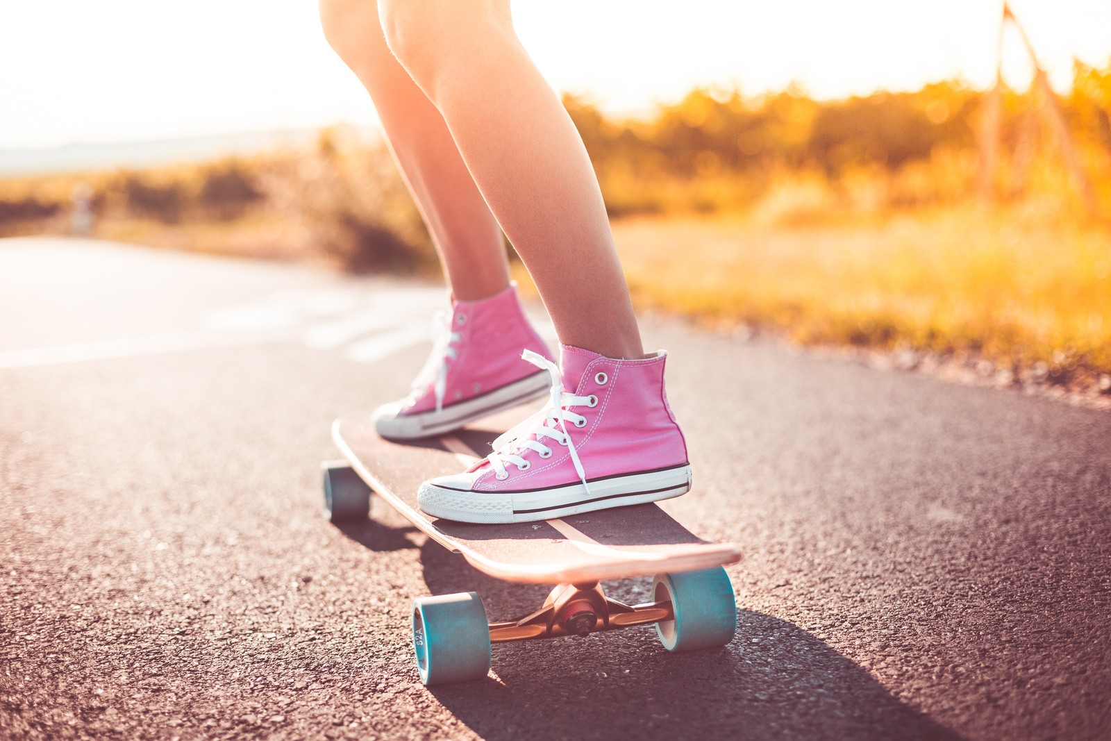 Eine giraffe auf einem skateboard auf einer straße mit einem feld im hintergrund (schuh, turnschuhe, schuhwerk, longboarding, longboard)