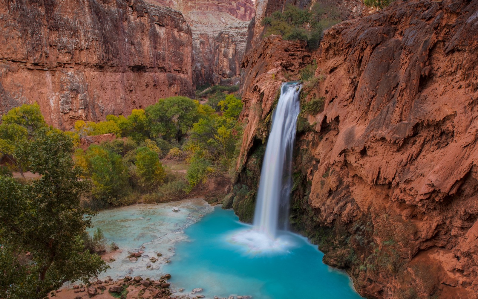 A waterfall flowing into a blue pool in the middle of a canyon (grand canyon, waterfall, canyon, body of water, water resources)