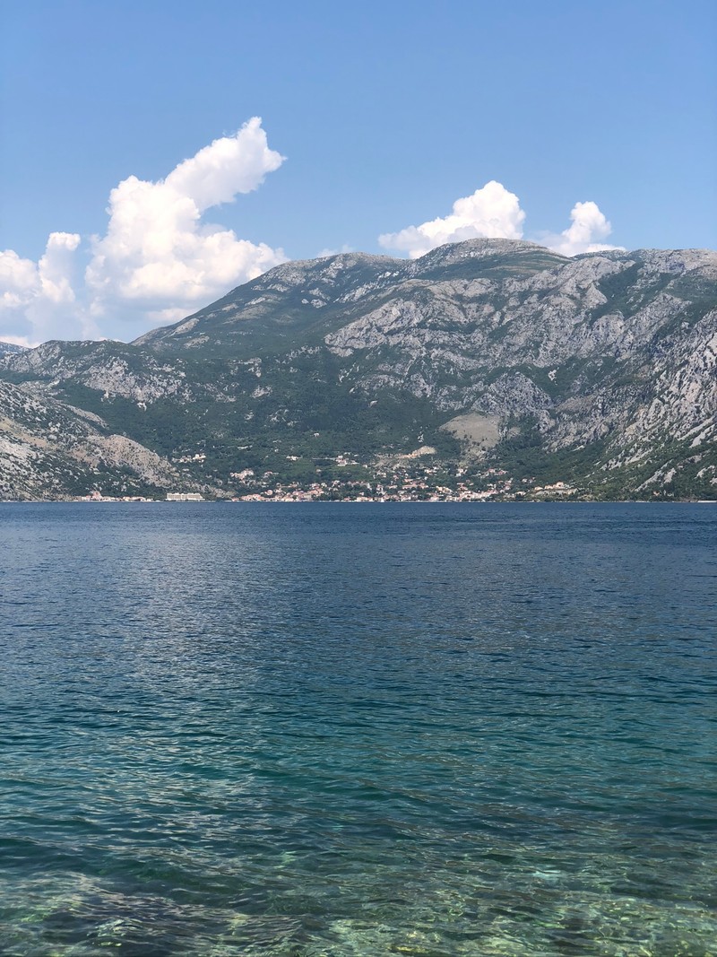 На картине изображена лодка, плавающая в воде у гор (море, горные образования, облако, водные ресурсы, горный хребет)