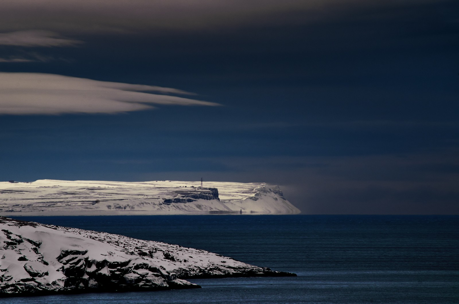 Un faro en una isla rocosa con una montaña nevada de fondo (océano ártico, iceberg, océano, mar, horizonte)