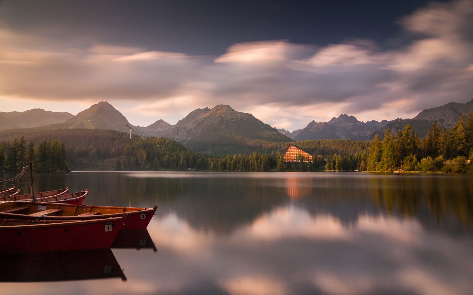 Barcos estão alinhados na beira de um lago com montanhas ao fundo (strbske pleso, parque nacional tatra, tatra national park, eslováquia, barcos)