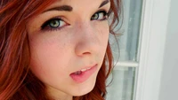 Close-up of a girl with vibrant red hair, striking green eyes, and freckles, showcasing natural beauty and soft features.