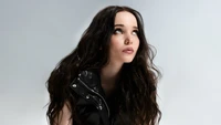 Dove Cameron em uma sessão de fotos impressionante, exibindo seu olhar expressivo e seu traje estiloso contra um fundo minimalista.