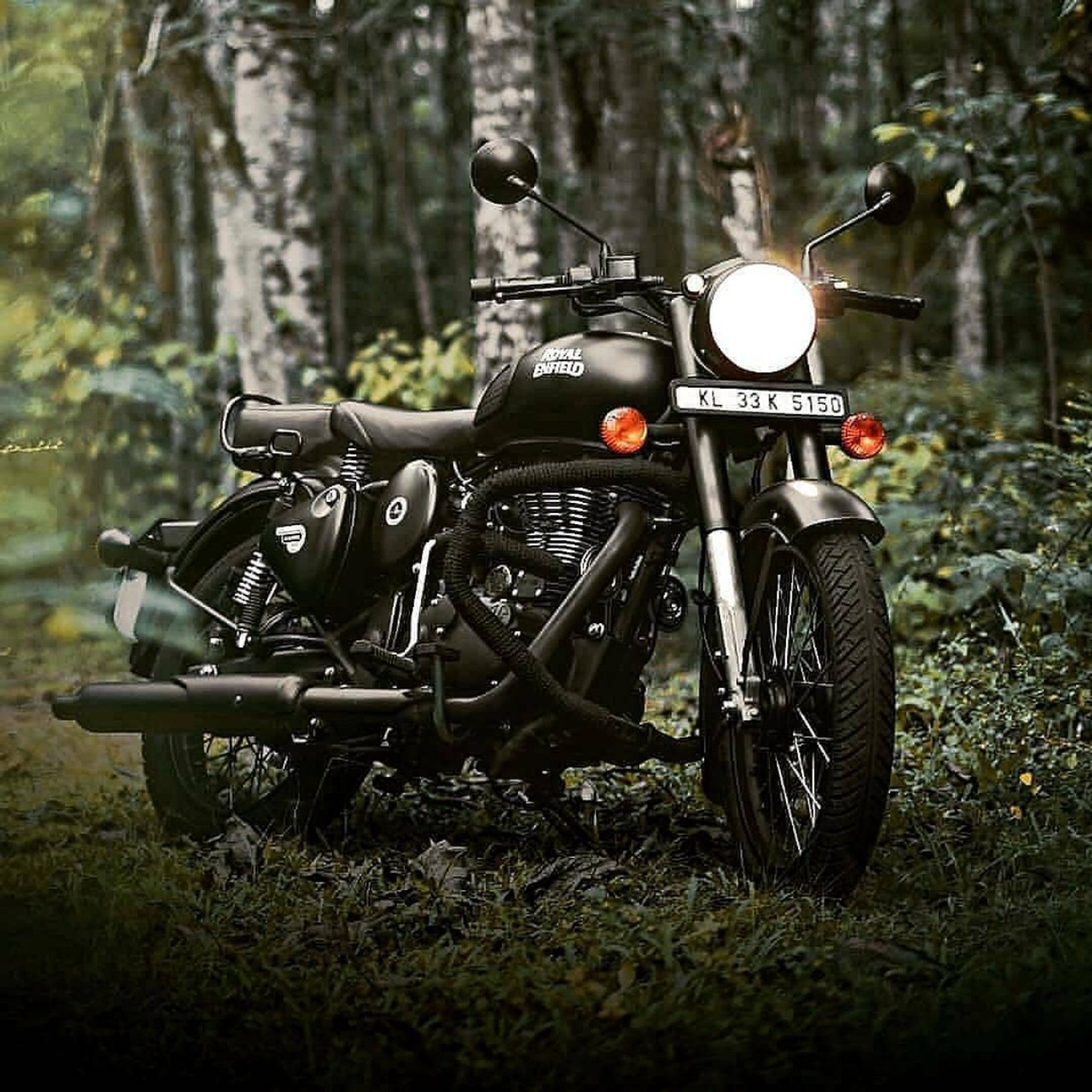 There is a motorcycle that is parked in the woods (500, classic, nature, royal enfield, stealth black)