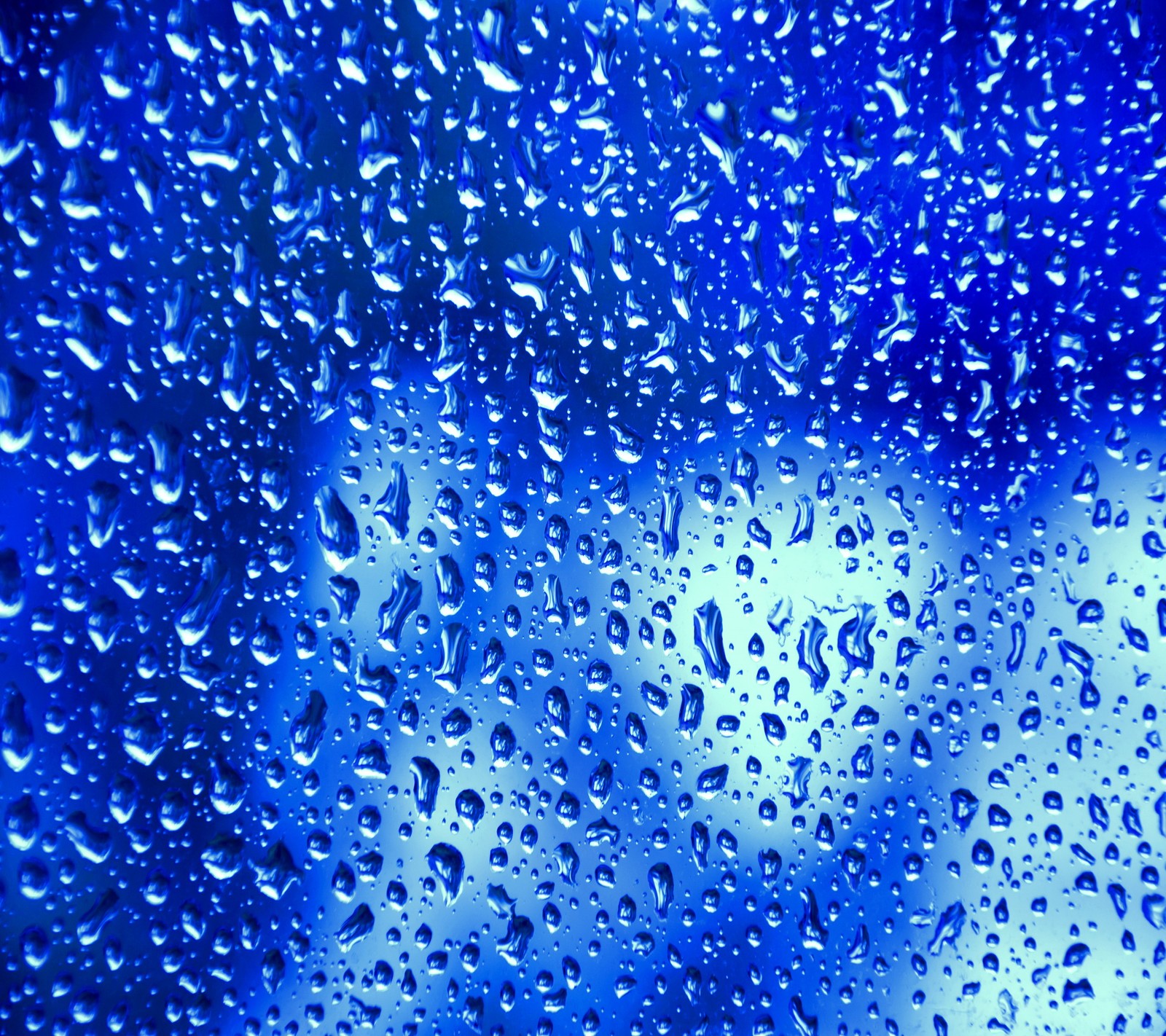 Un gros plan d'une fenêtre couverte de pluie avec des gouttes d'eau (blue rain drops, water window abstract)