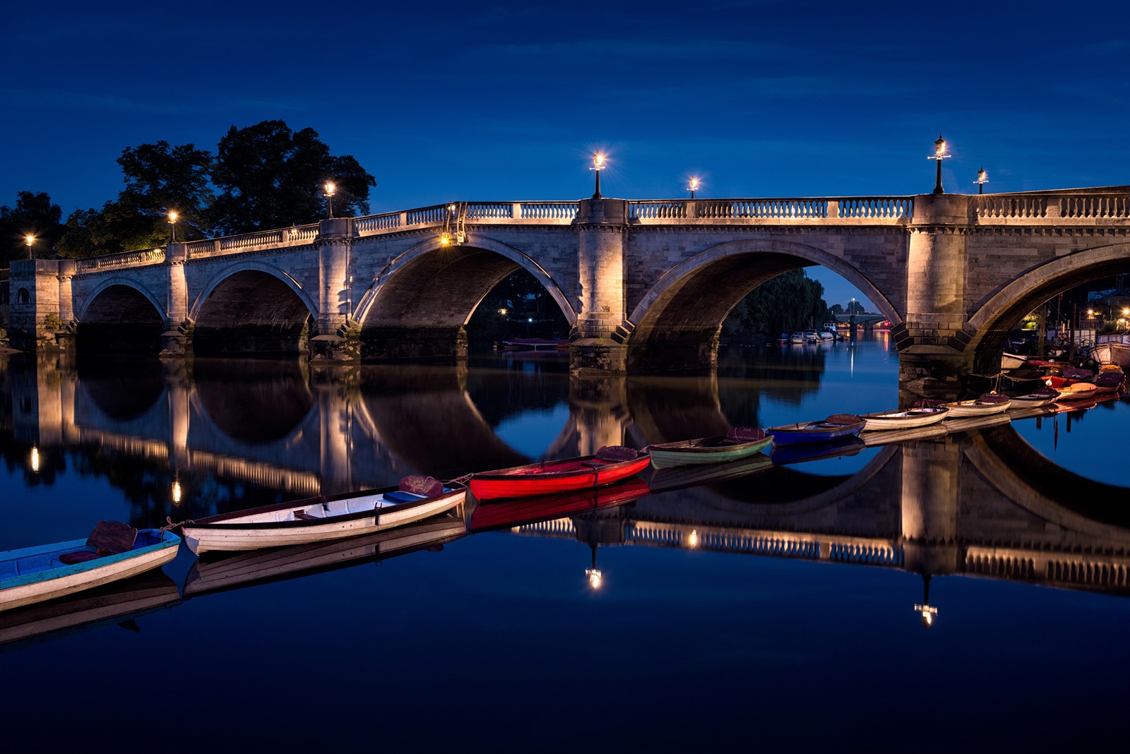 Des bateaux sont alignés sur l'eau devant un pont (réflexion, pont, point de repère, nuit, eau)