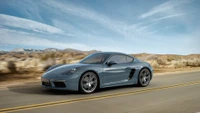 Porsche 718 Cayman en mouvement sur une route désertique pittoresque.