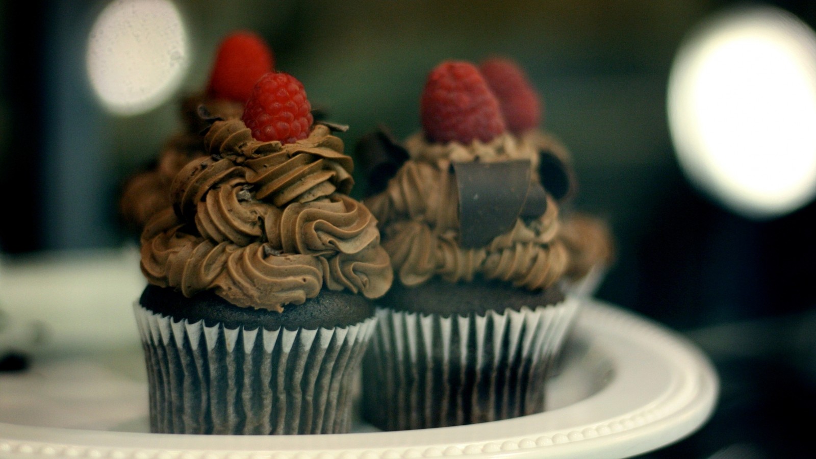 Zwei cupcakes auf einem teller mit schokoladenglasur und himbeeren (buttercreme, zuckerguss, essen, süße, backen)