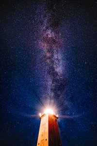 Un phare illuminé sur fond de Voie lactée, entouré d'un ciel nocturne étoilé, fusionnant la beauté de la structure humaine avec l'immensité du cosmos.