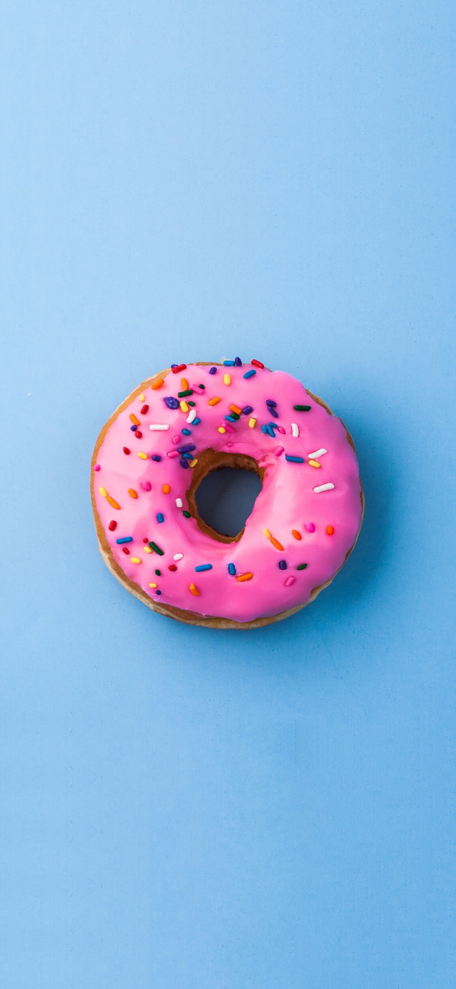 Una dona rosa con chispas en una superficie azul (labio, comida, donut, productos horneados, círculo)