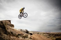 A mountain biker performing a jump over rugged terrain against a dramatic sky, showcasing the thrill of extreme sports in Moab.