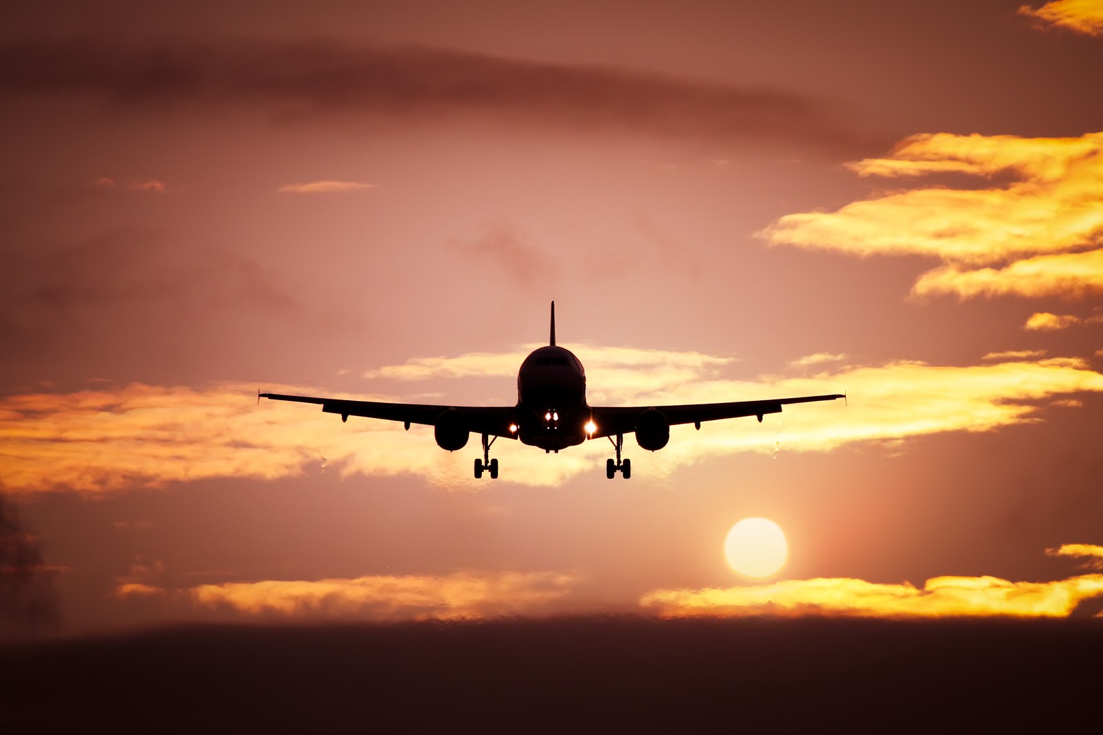 Um avião voando no céu ao pôr do sol com o sol atrás dele (aeronave, aeroporto, viagem aérea, linha aérea, aviação)