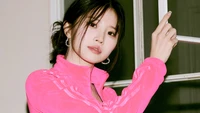 Hayoung de fromis_9 présente un look vibrant dans une tenue rose, dégageant une présence charmante sur un fond doux et neutre.