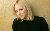 A smiling girl with long blond hair and soft features, posing against a textured gold background.