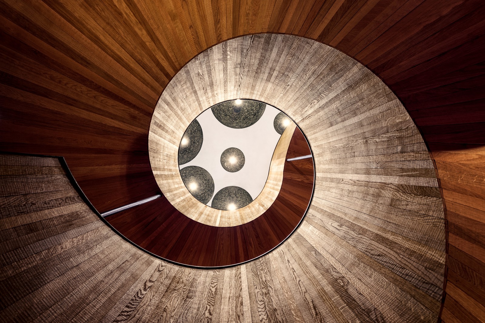 Vue d'un escalier en colimaçon avec un luminaire circulaire (escalier en colimaçon, escaliers en bois, hôtel, courbes, lumières)