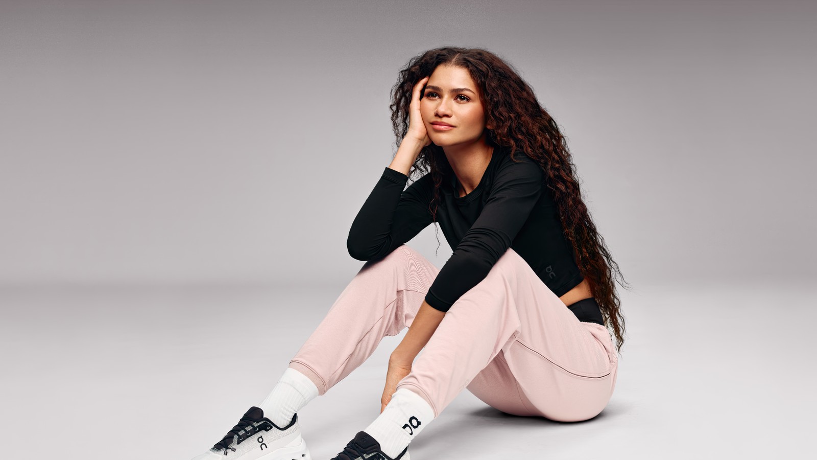 Une femme assise par terre en pantalon rose et haut noir (zendaya, sourire, 2024, actrice américaine, gens)