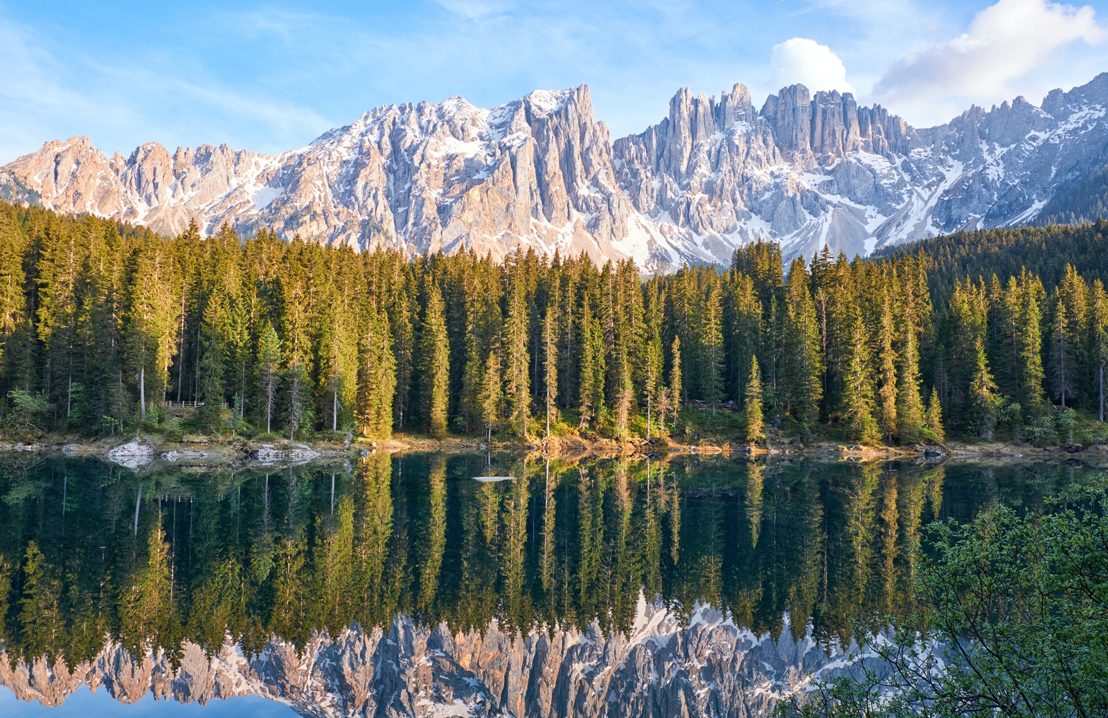 A view of a lake surrounded by trees and mountains (karersee lake, latemar, mountain range, snow covered, reflection)