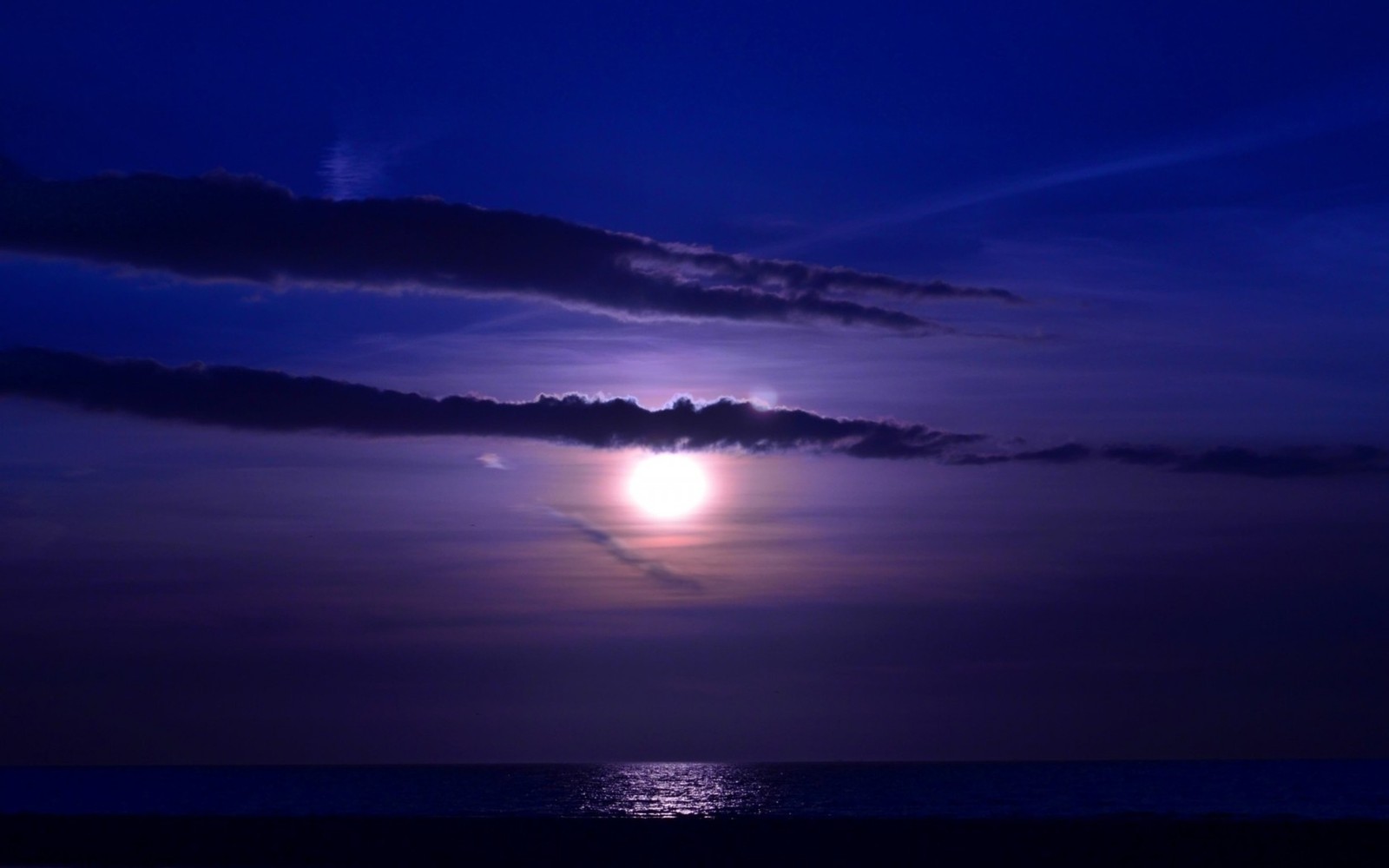 Une vue d'une pleine lune se couchant sur l'océan avec des nuages (clair de lune, horizon, mer, nuage, ciel)