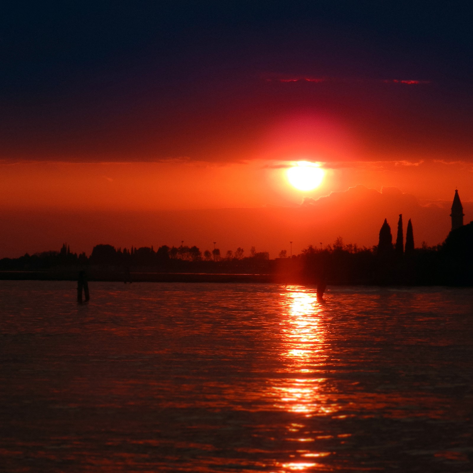 Sunset over a body of water with a person standing in the water (afterglow, water, atmosphere, water resources, amber)