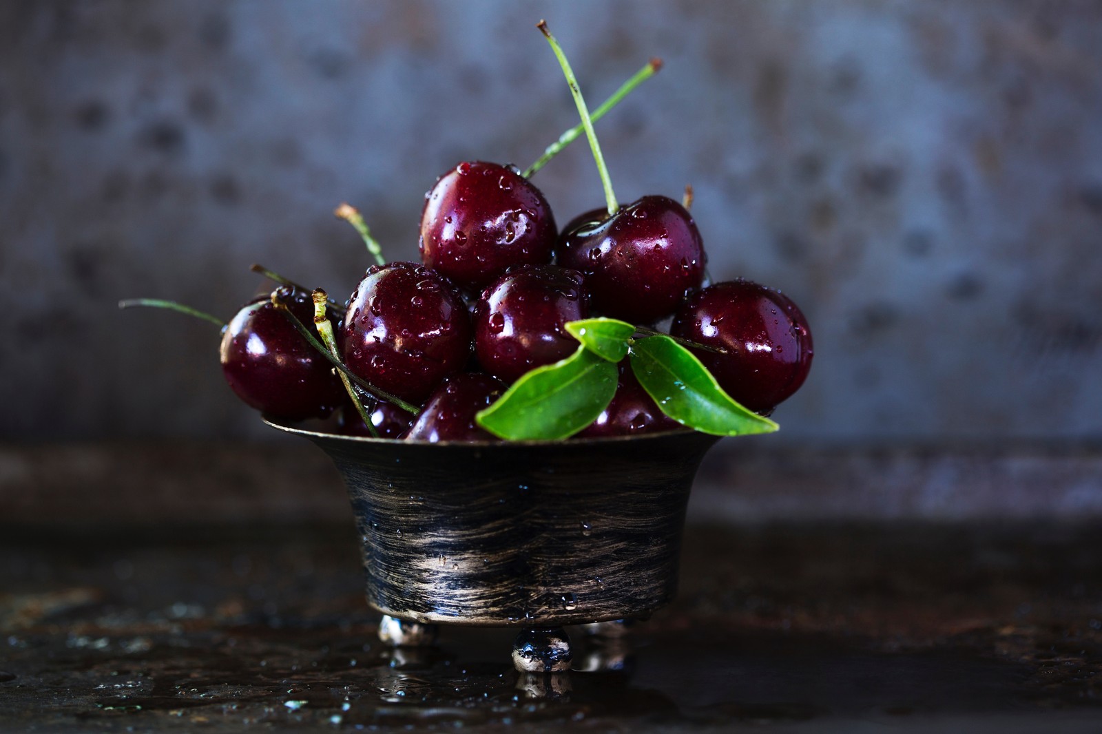 There is a bowl of cherries with leaves on a table (cherry, fruit, food, plant, cranberry)