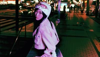 Giselle de aespa pose avec style dans un cadre urbain vibrant, mettant en avant un mélange de mode K-pop et d'ambiance nocturne.