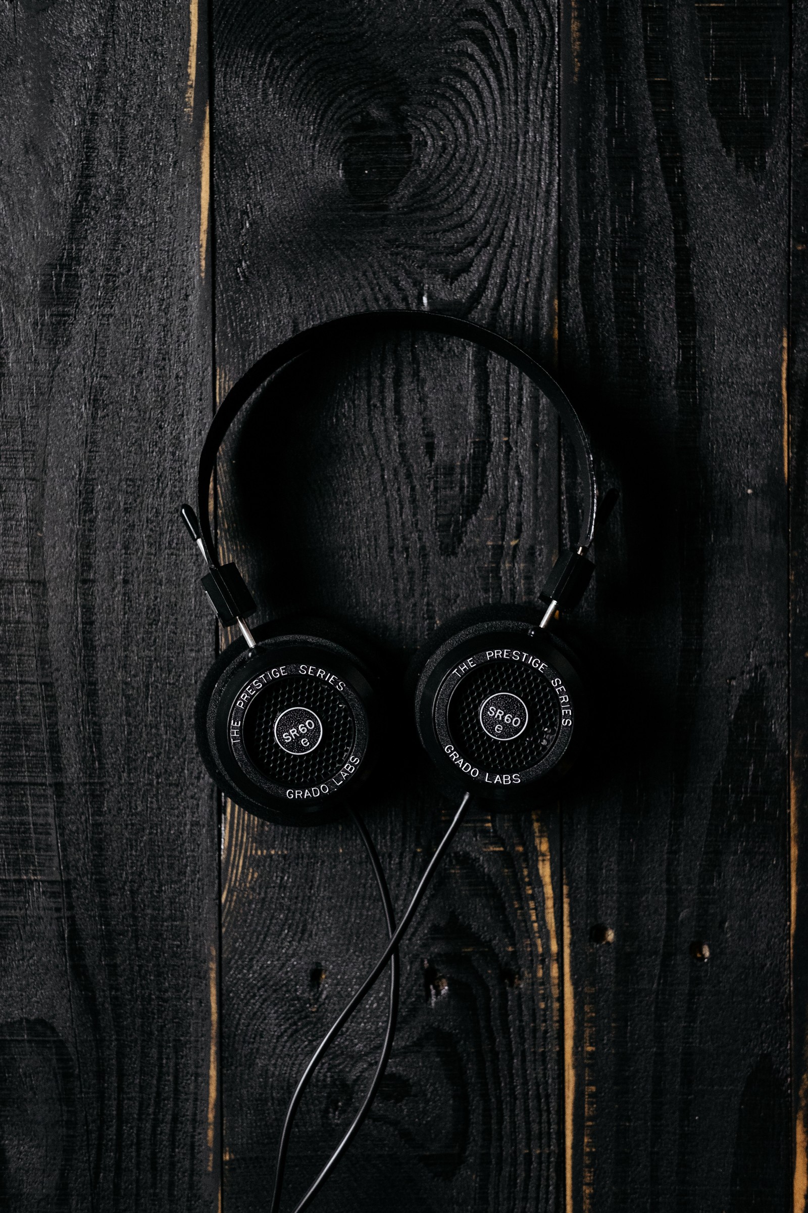 A close up of a pair of headphones on a wooden surface (headphones, headset, black, audio equipment, technology)