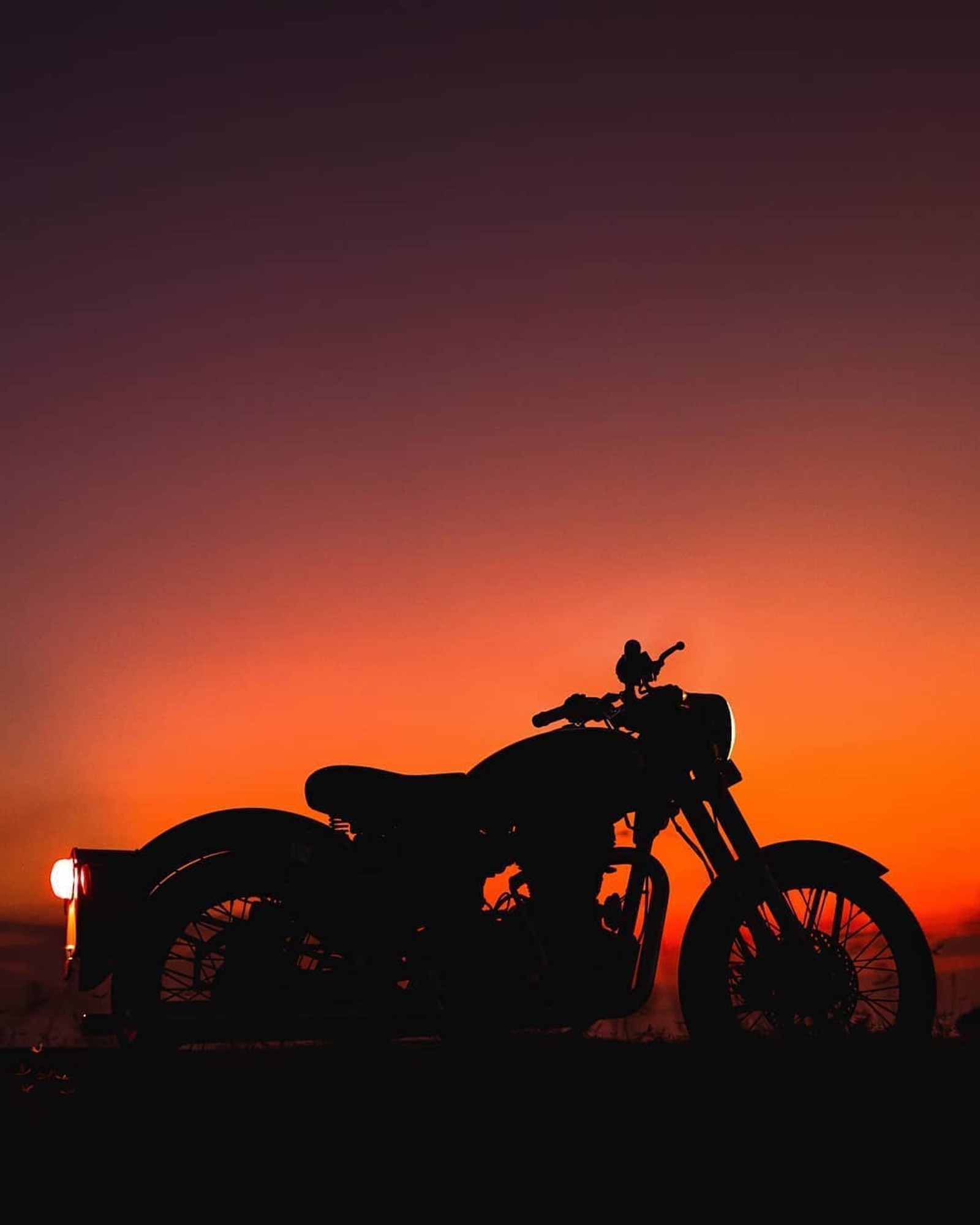 Arafed motorcycle parked on a hill at sunset with a bright orange sky (enfield, royal)