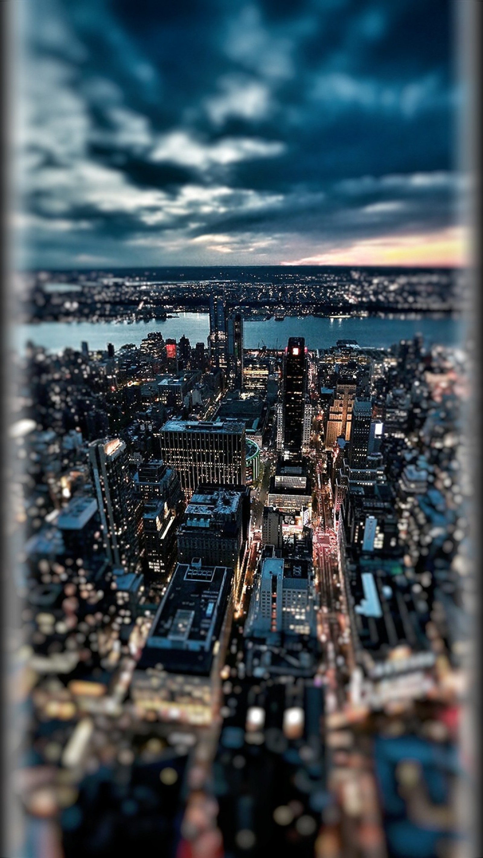 Uma vista aérea de uma cidade à noite com um rio ao fundo (bonito, cidade, colorido, nuvens escuras, estilo de borda)