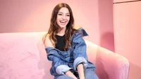 Celine Farach souriante dans une tenue en denim décontractée sur un canapé rose