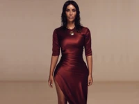 Kim Kardashian in a sleek burgundy dress against a warm brown background.