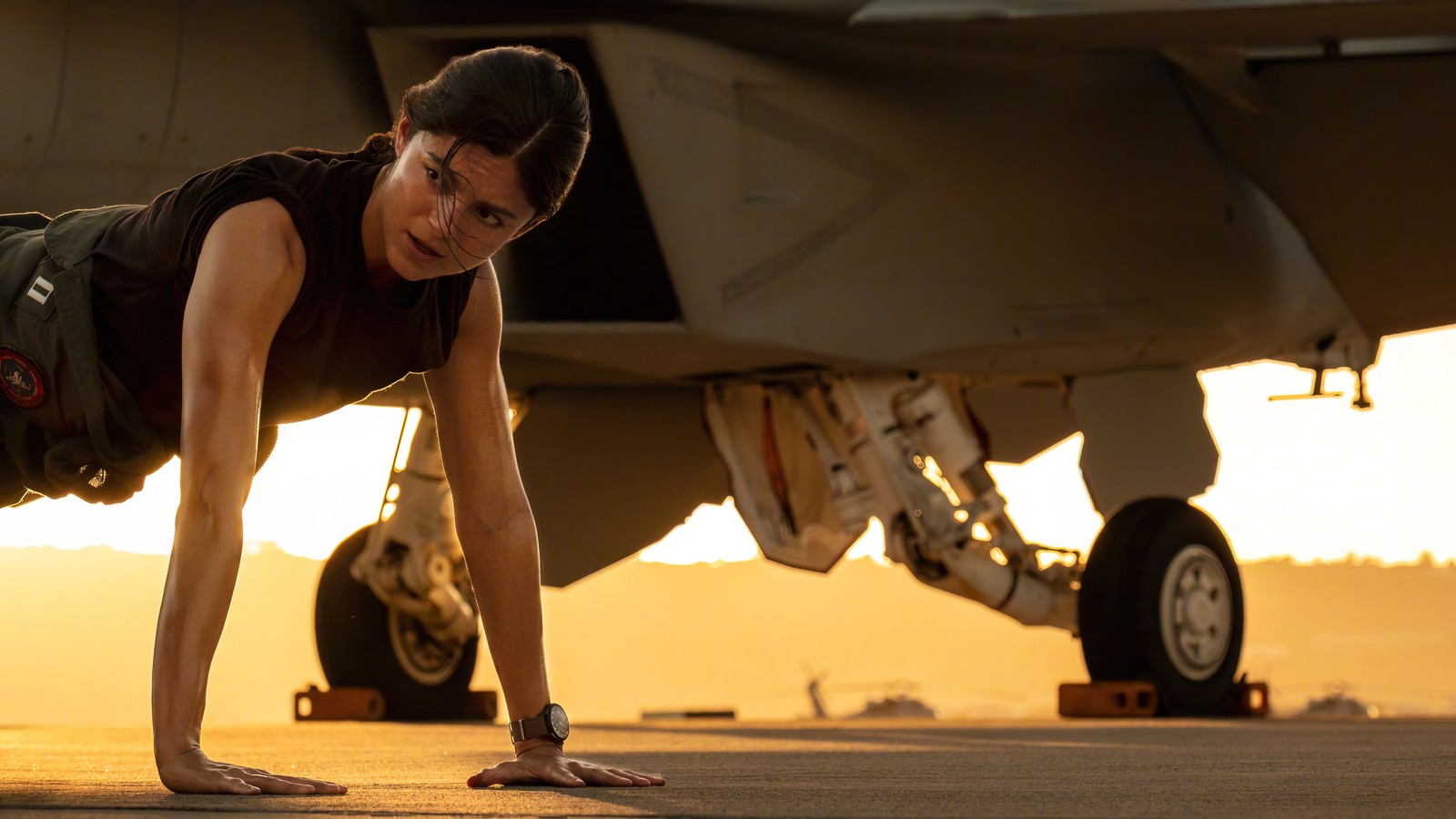 Une femme faisant des pompes sur une piste devant un chasseur (top gun maverick, 2022, film, monica barbaro)