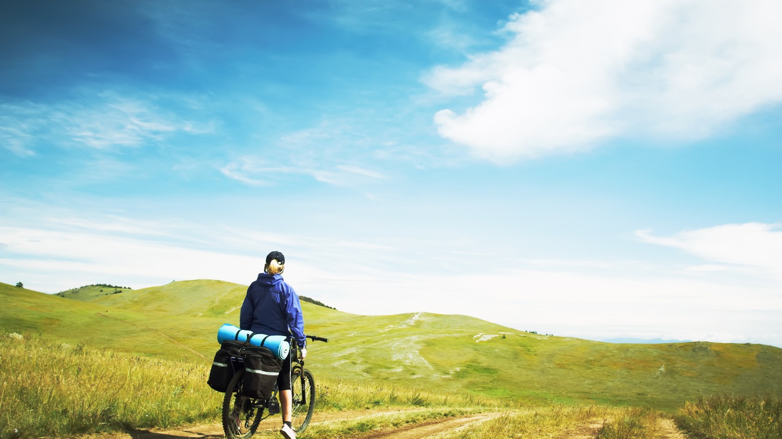 There is a man riding a bike on a dirt road (cycling, bicycle, cloud, clouds, hill)