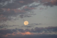 Lever de soleil pastel avec une pleine lune parmi des nuages doux