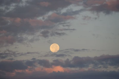 Amanecer pastel con una luna llena entre nubes suaves