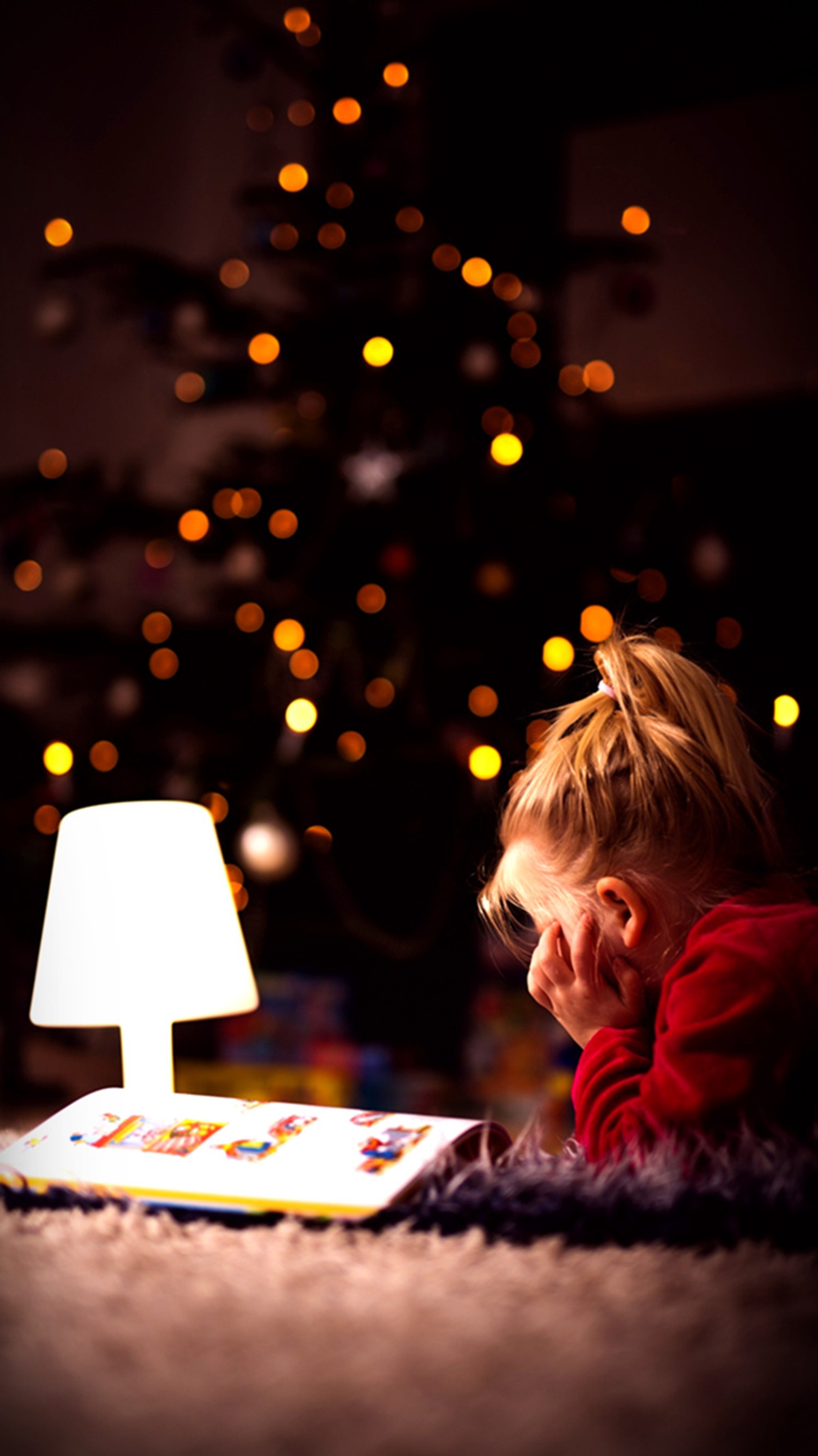 Arafed child reading a book in front of a christmas tree (baby, balls, christmas, lights, stories)