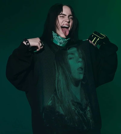 Billie Eilish mostrando un atrevido sudadera de gran tamaño con su propia imagen, contra un fondo verde.