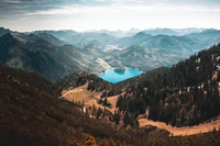 Majestuosa cordillera montañosa con un sereno lago enclavado en un exuberante valle, rodeado de árboles imponentes y una vasta naturaleza salvaje.