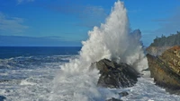 Breaking Waves Crash Against Rocky Coastline Under Blue Skies