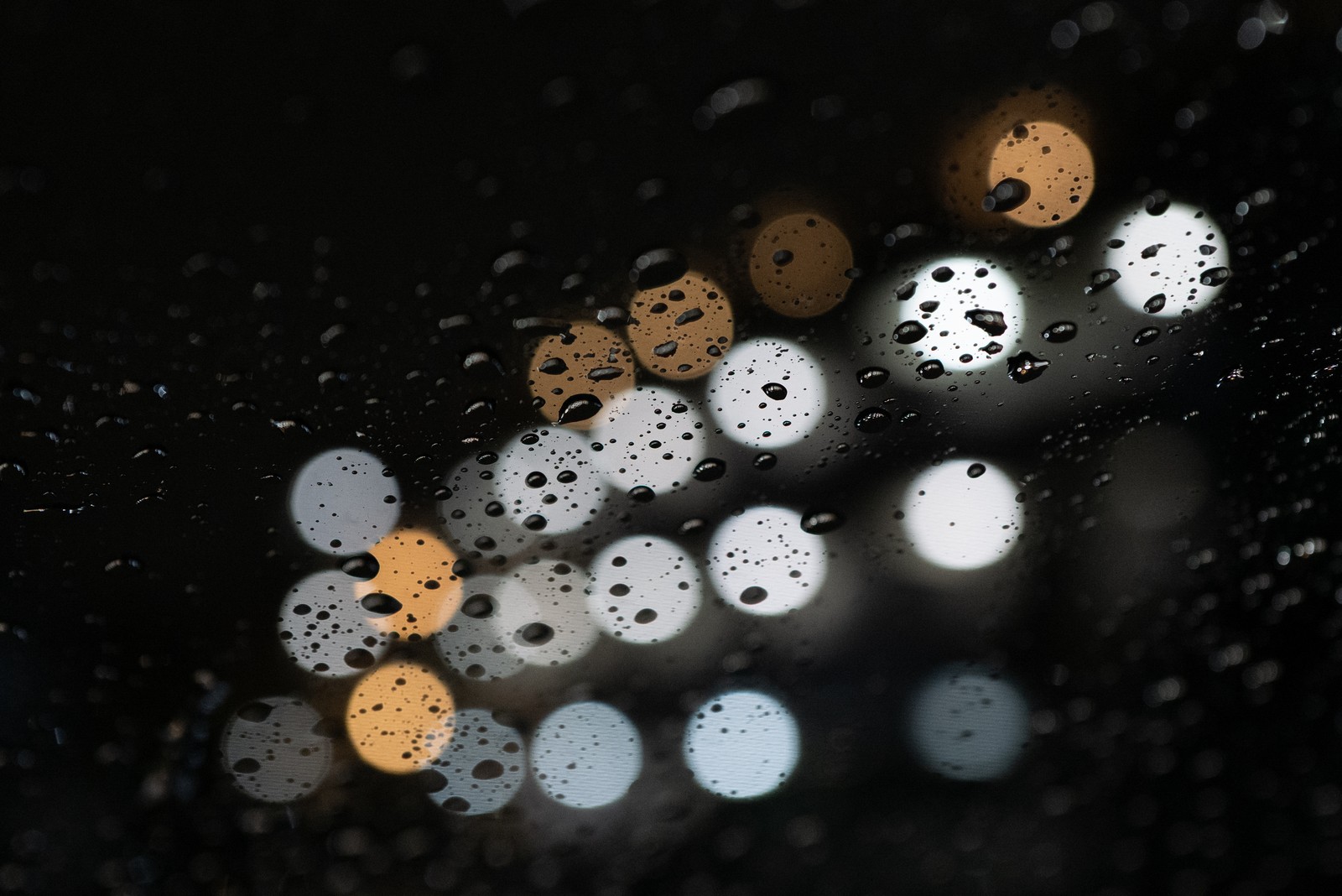 Nahaufnahme eines regennassen fensters mit einer straßenlaterne im hintergrund (knopf, kreis, reflexion, meter, macro)