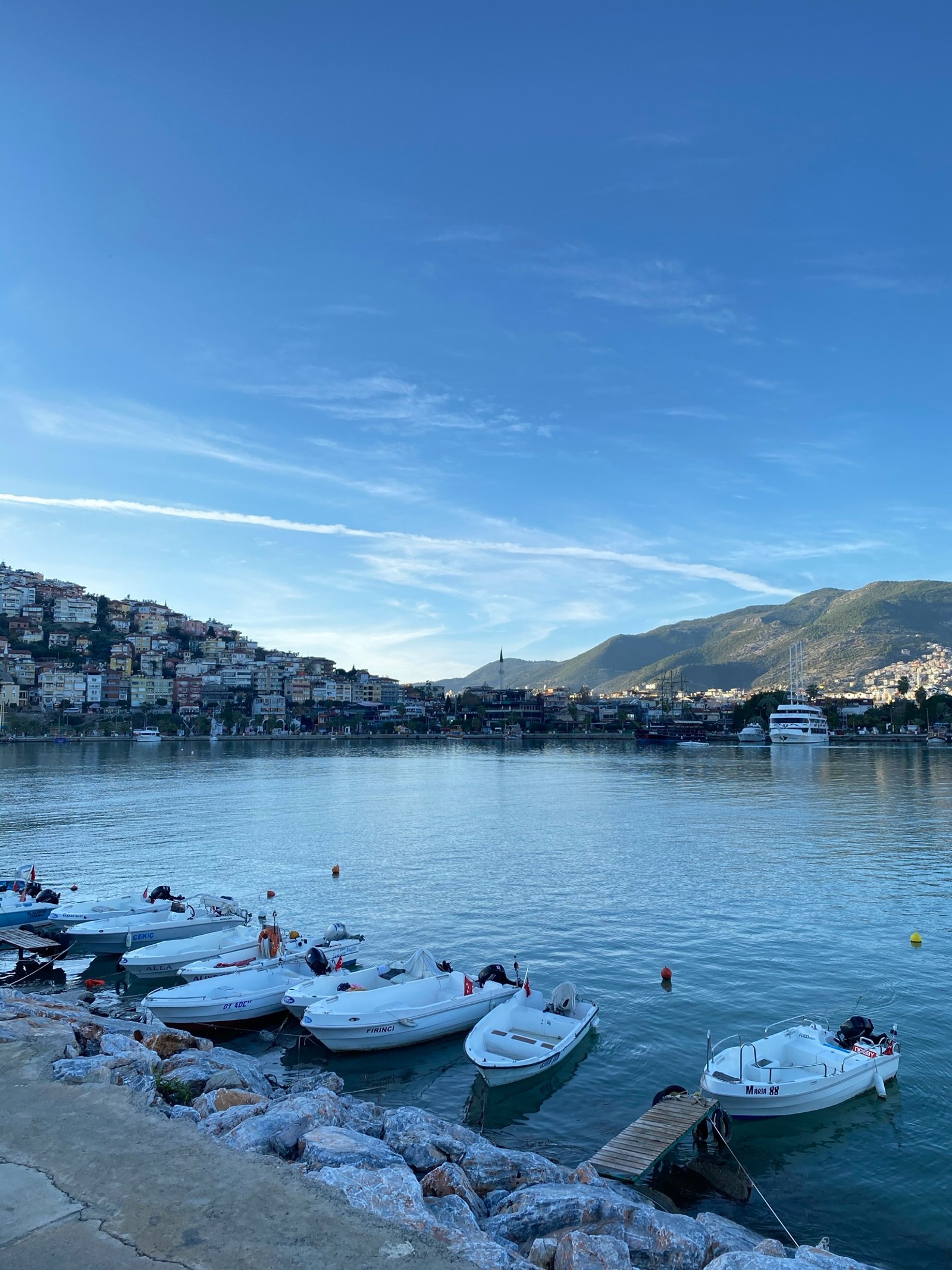 Os barcos estão atracados em um píer em uma baía com uma montanha ao fundo. (água, nuvem, barco, recursos hídricos, embarcação)