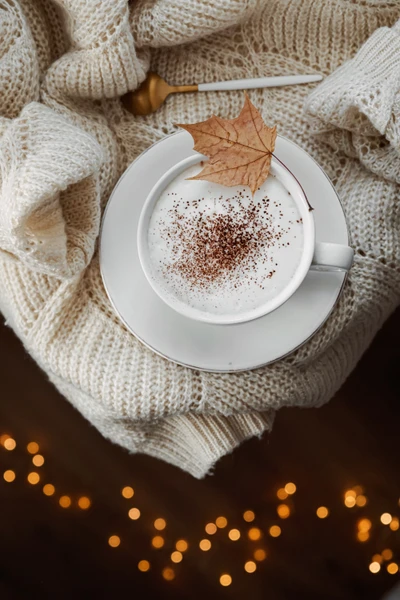 Latte aconchegante com folha de outono em um fundo de malha macia