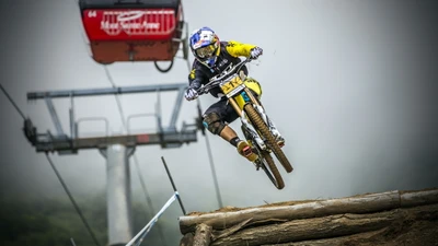 Ciclista de montanha descendo, saltando de uma rampa com um teleférico ao fundo