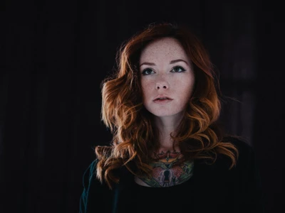 Portrait of a woman with striking red hair and intricate tattoos, exuding beauty and confidence.